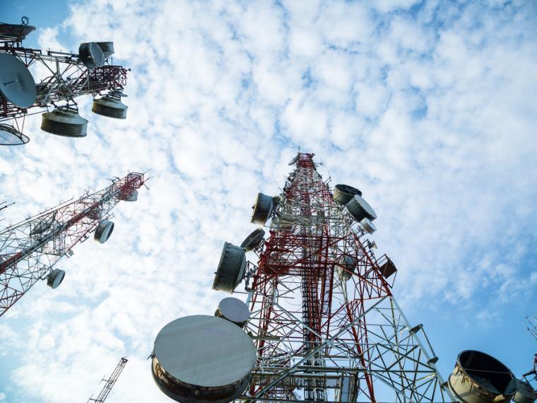 Looking up at multiple radio towers from the base